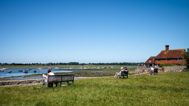 People sit on benches overlooking Chichester Harbor at Bosham in West Sussex, UK. (Photo by: Andy Soloman/UCG/Universal Images Group via Getty Images)