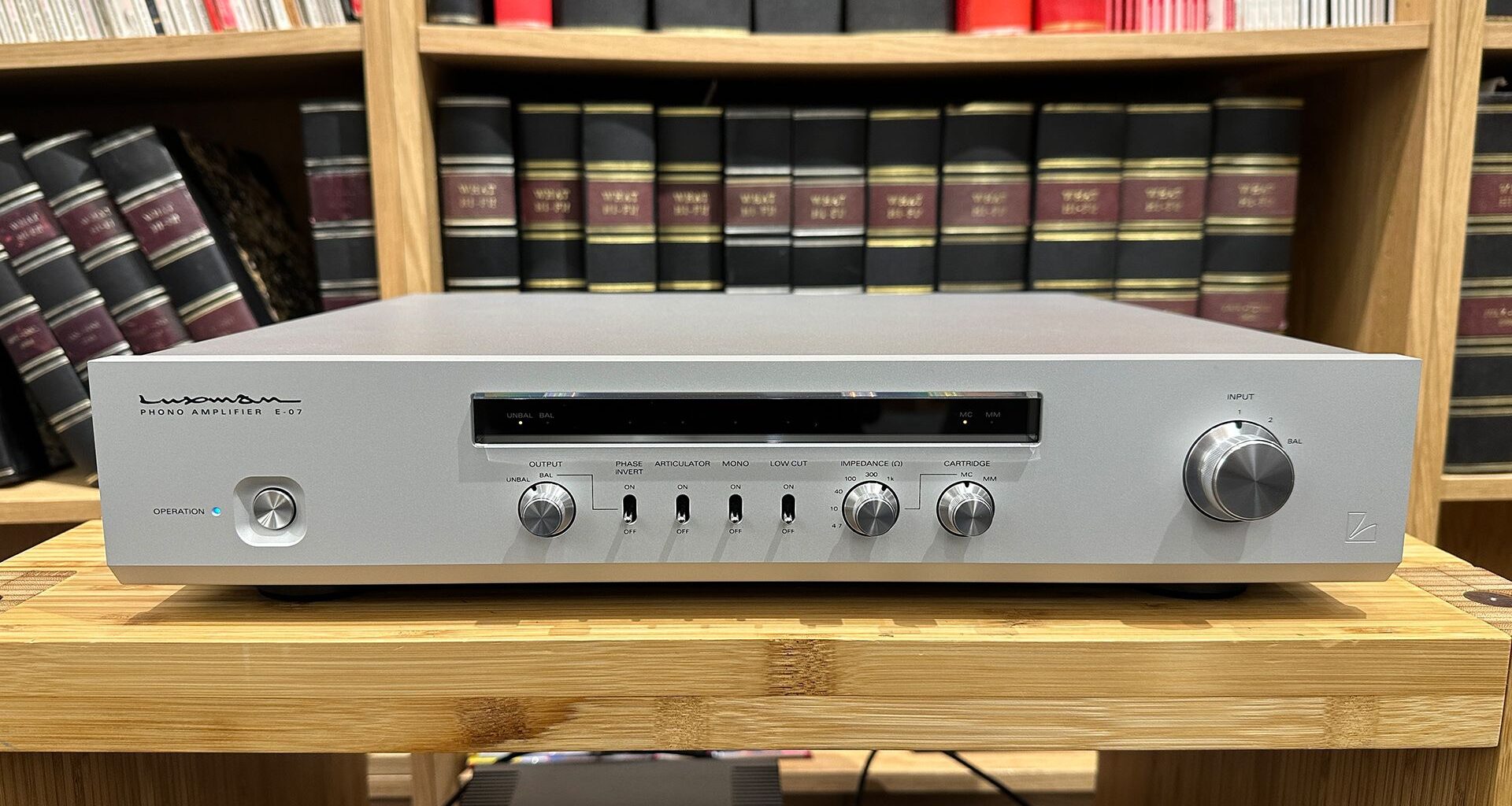 Luxman E-07 phono stage on wooden hi-fi rack in front of bookcase