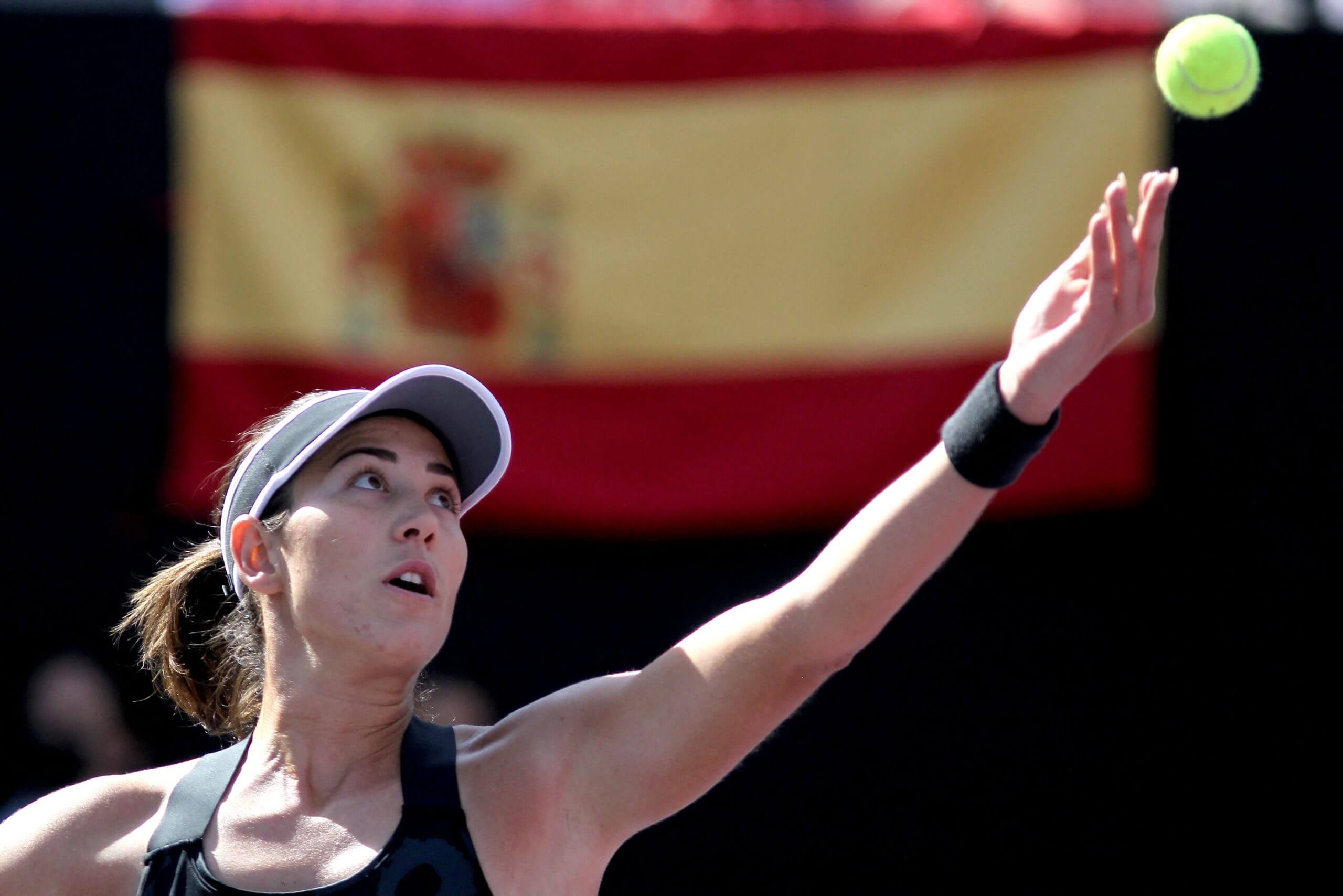 Garbiñe Muguruza prepares to serve with a Spanish flag behind her.