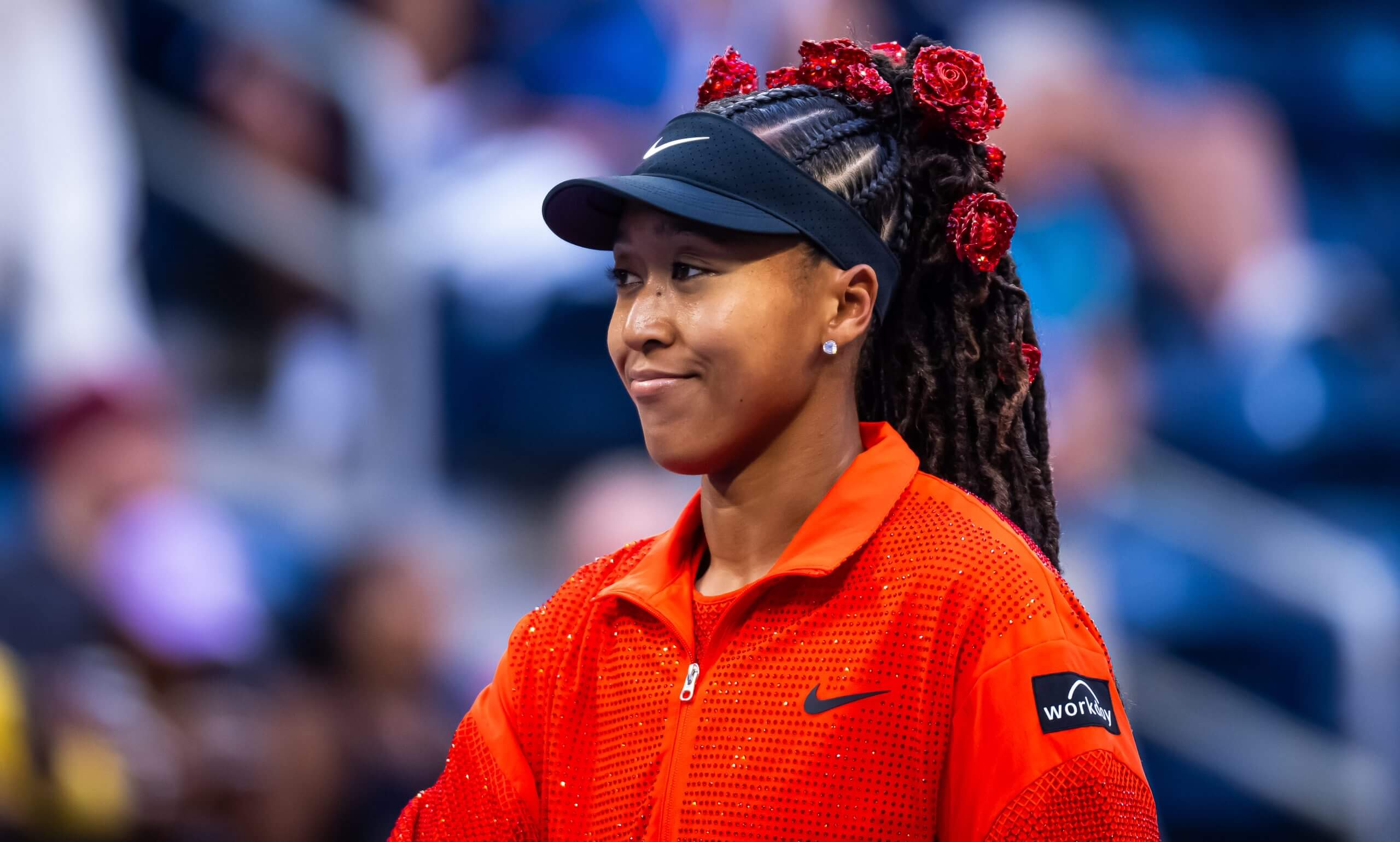 Naomi Osaka walks on wearing a red, glittering jacket and a red-rose hairpiece.