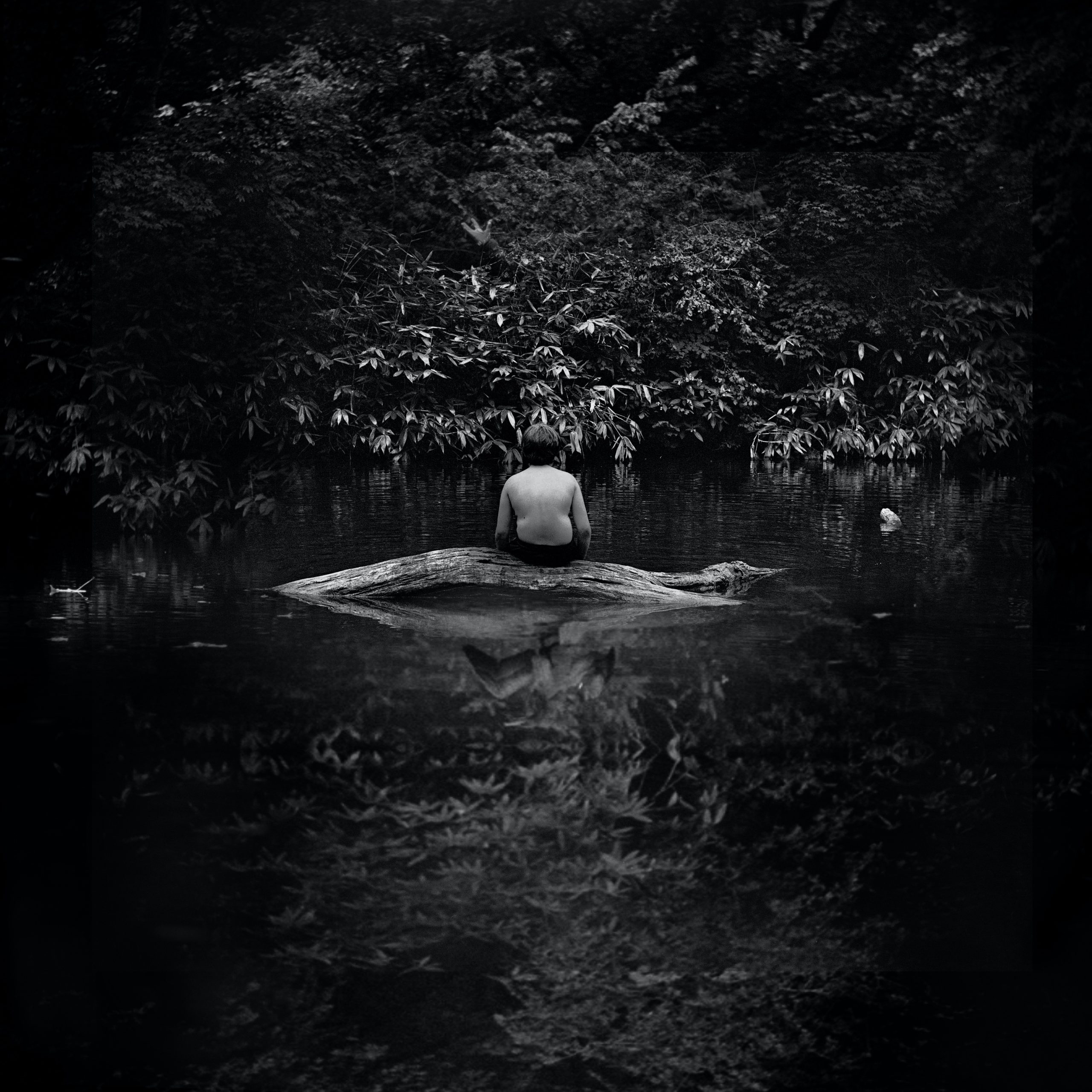 A boy sits alone on a log in a river. 