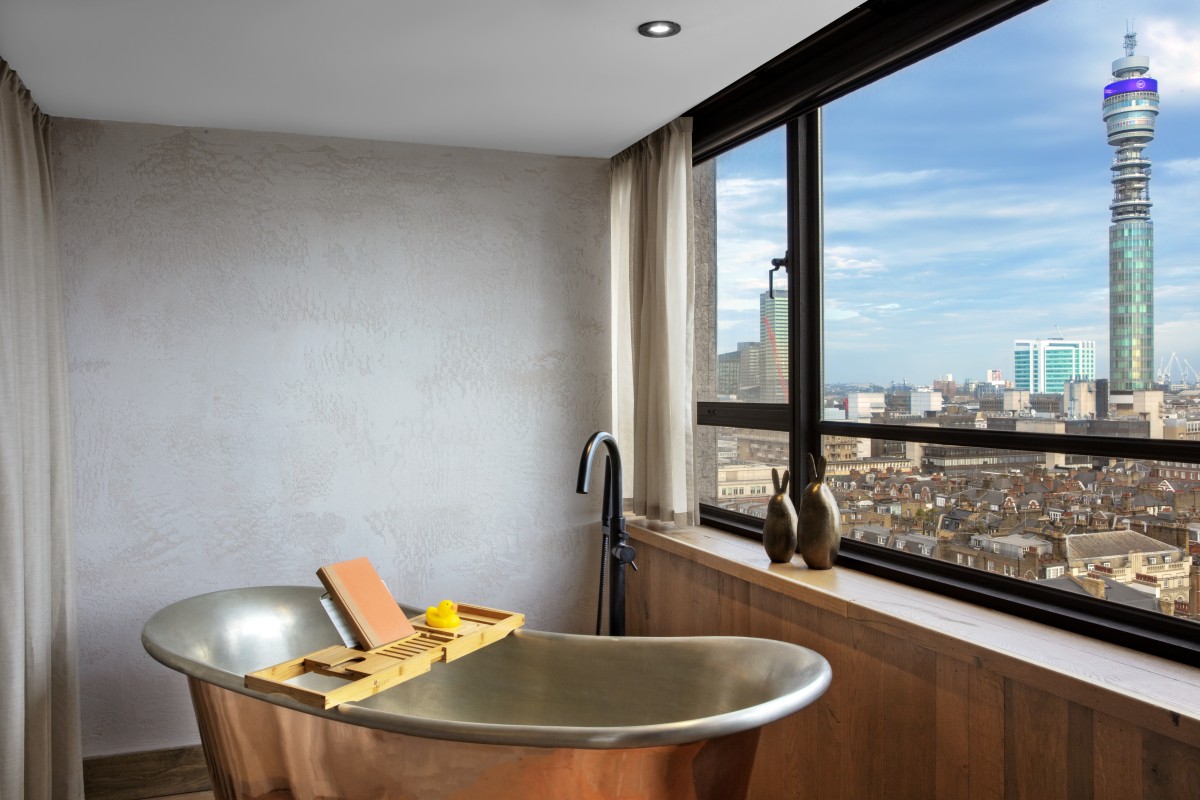 A free standing bath next to a window, looking out onto a view of London with the BT Tower in the background