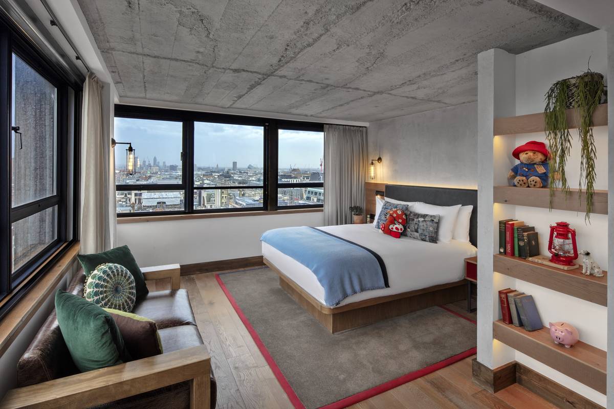 A bed and window seat in a hotel room at Treehouse, looking out onto a sweeping view of London