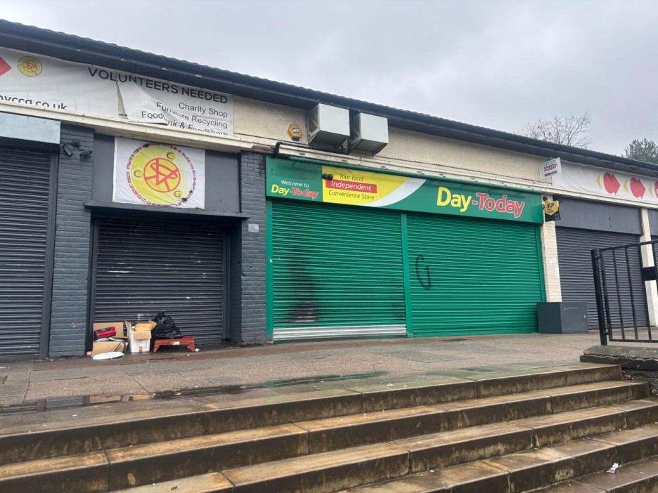 Exterior of a Day-Today convenience store and a charity shop with closed shutters.