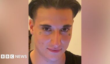 Image of Aidan Chapman looking at the camera, a man with dark floppy hair and a tattoo under each eye - one of a broken heart and the other the number 13