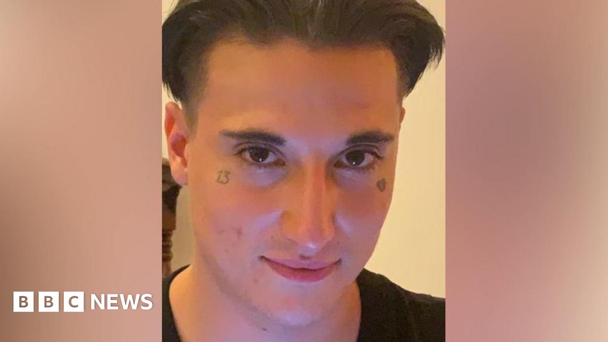 Image of Aidan Chapman looking at the camera, a man with dark floppy hair and a tattoo under each eye - one of a broken heart and the other the number 13