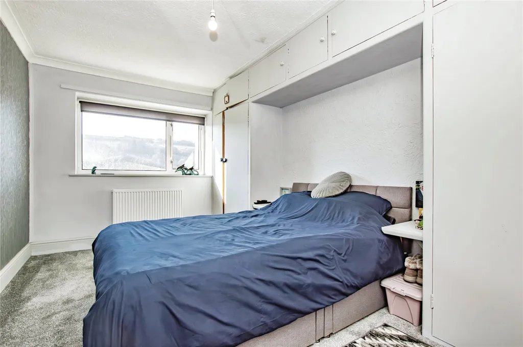 Bedroom with overhead cabinets, blue duvet, window and radiator in a clean, modern layout.