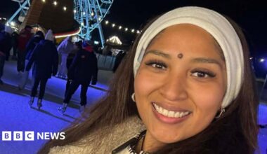Joyce Leon Velasquez smiles at the camera on an ice rink at Christmas time. She has a white headband on and black coat. People can be seen ice skating behind her. There is also a large Ferris wheel that is lit up.