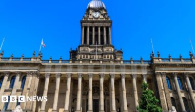 The front of the Victorian Leeds Town Hall. The stone building has large pillars supporting the roof with a large clock tower abover