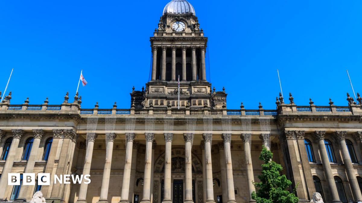 The front of the Victorian Leeds Town Hall. The stone building has large pillars supporting the roof with a large clock tower abover