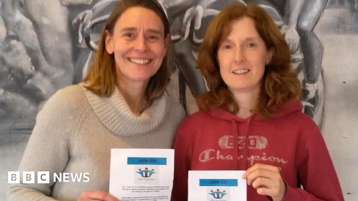 Two women, one in a red hoodie and one in a cream sweater, pose together smiling and holding up a white certificate for the camera