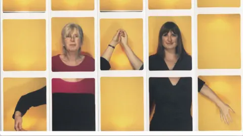 Kate Tyler A collage of photo booth strips. The overall image has a yellow background, there are white lines where the strips begin. On the left is an older woman wearing a red and black top and glasses, she is holding hands with the woman on the right, who has shoulder length brown hair and is wearing a dress. They are both looking forward. 