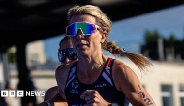 Zoe Tucker competing with a blue GBR running vest, the number 1720 on her arm, and a stadium of spectators behind her.