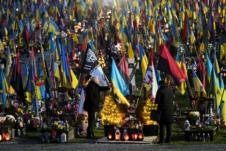 People visit the graves of fallen Ukrainian soldiers decorated with Christmas trees and New Year's decorations at the Lychakiv Military Cemetery, on the day before Christmas Eve, in Lviv on December 23, 2025, amid the Russian invasion of Ukraine. (Photo by YURIY DYACHYSHYN / AFP)