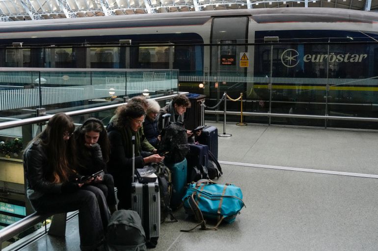 Travellers sit with their bags next to a Eurostar train at St. Pancras station in London on December 30, 2025, as Eurostar train service between Britain and continental Europe is halted.