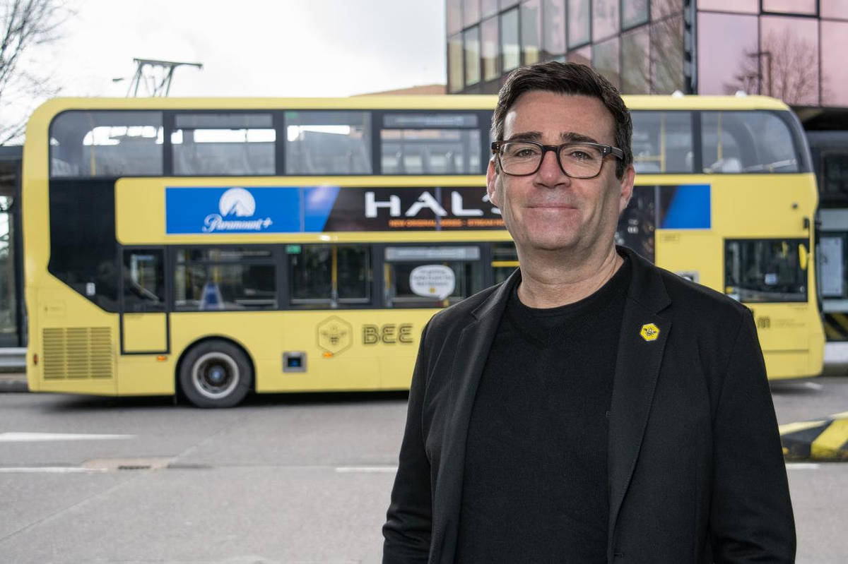 andy burnham, mayor of greater manchester, stood in front of yellow bee network bus