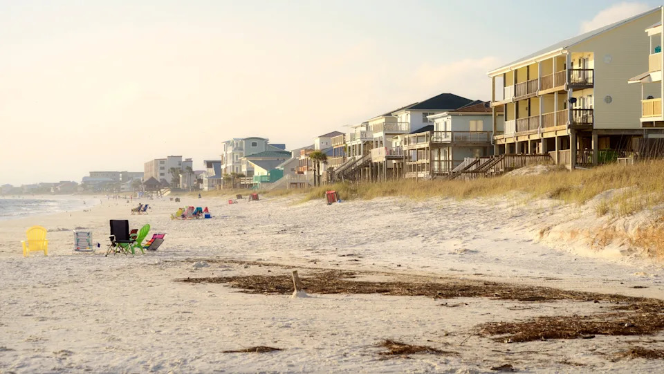 Beachfront properties with balconies overlook a sandy beach with scattered chairs and people enjoying the shoreline