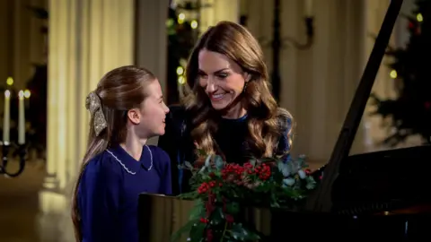 Kensington Palace Princess Charlotte and Catherine, The Princess of Wales, sit smiling at a piano as they perform at for a Christmas Carol service