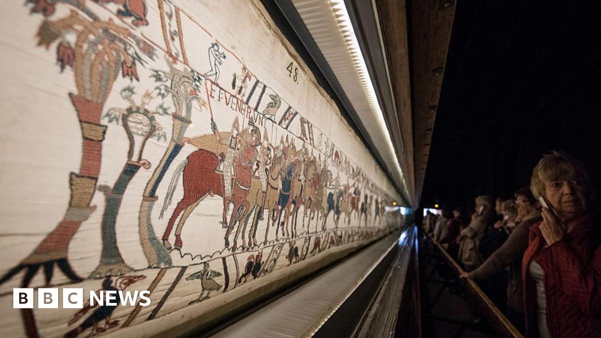 A photograph of people inspecting the Bayeux Tapestry in an art gallery