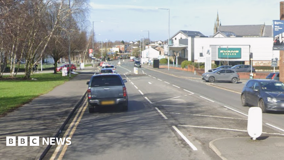 Google streetview of cars driving on North Road with trees on left and shops and properties on right