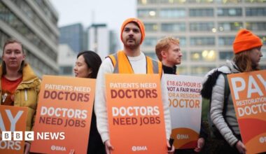 Resident doctors wearing orange beanie hats and carrying orange placards bearing the wears Doctor Need Jobs