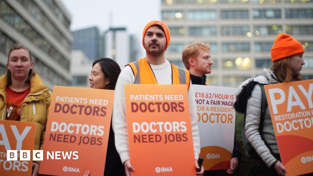 Resident doctors wearing orange beanie hats and carrying orange placards bearing the wears Doctor Need Jobs