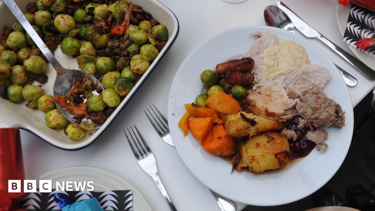 A roast dinner on a white plate, with meat, potatoes and vegetables. Next to it is  a dish of sprouts with a serving spoon.
