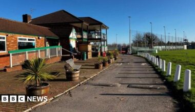 A pub seen from the outside next to a green field. The sky is blue and the sun is shining.