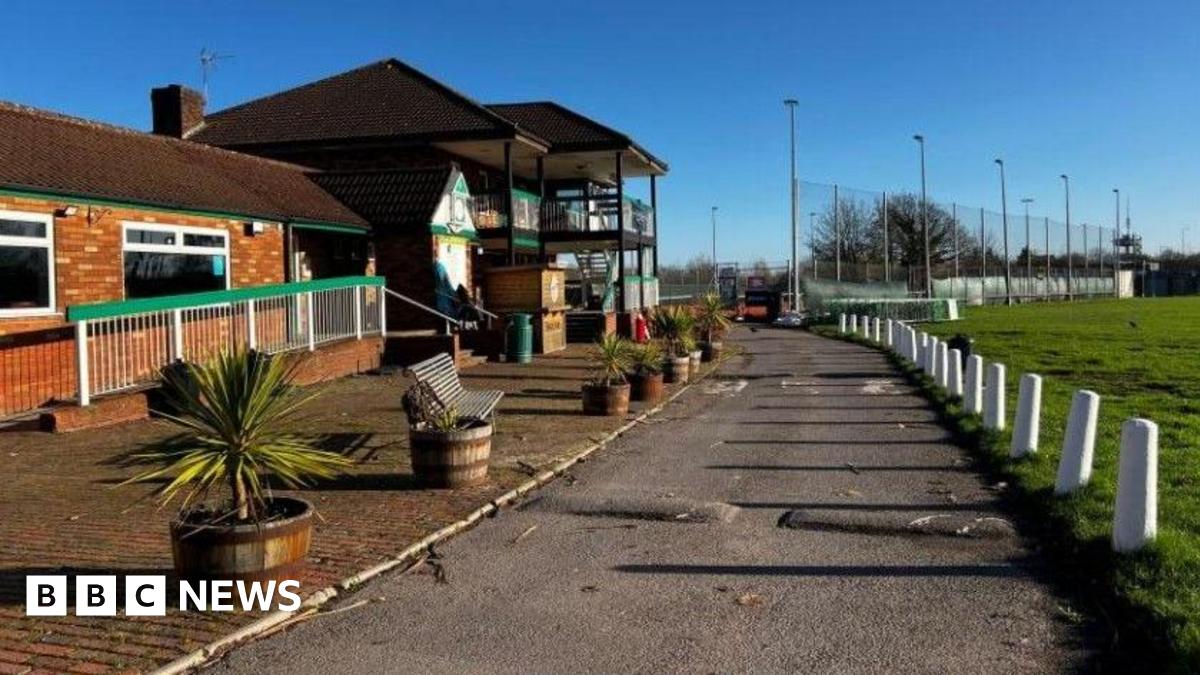 A pub seen from the outside next to a green field. The sky is blue and the sun is shining.