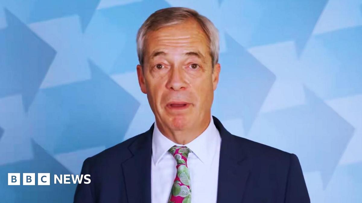 Nigel Farage looks into the camera mid-speech while standing in front of a backdrop with blue arrows. He is wearing a navy blue blazer, a pink tie with a lime print and a white shirt.