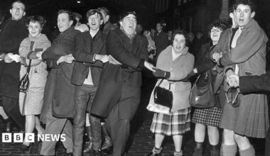 A black and white photo of people singing Auld Lang's Syne during New Year at the Tron, Edinburgh 1964.
