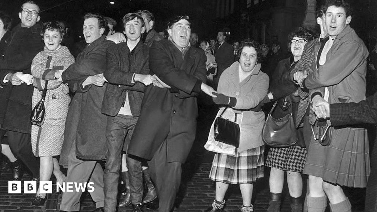 A black and white photo of people singing Auld Lang's Syne during New Year at the Tron, Edinburgh 1964.