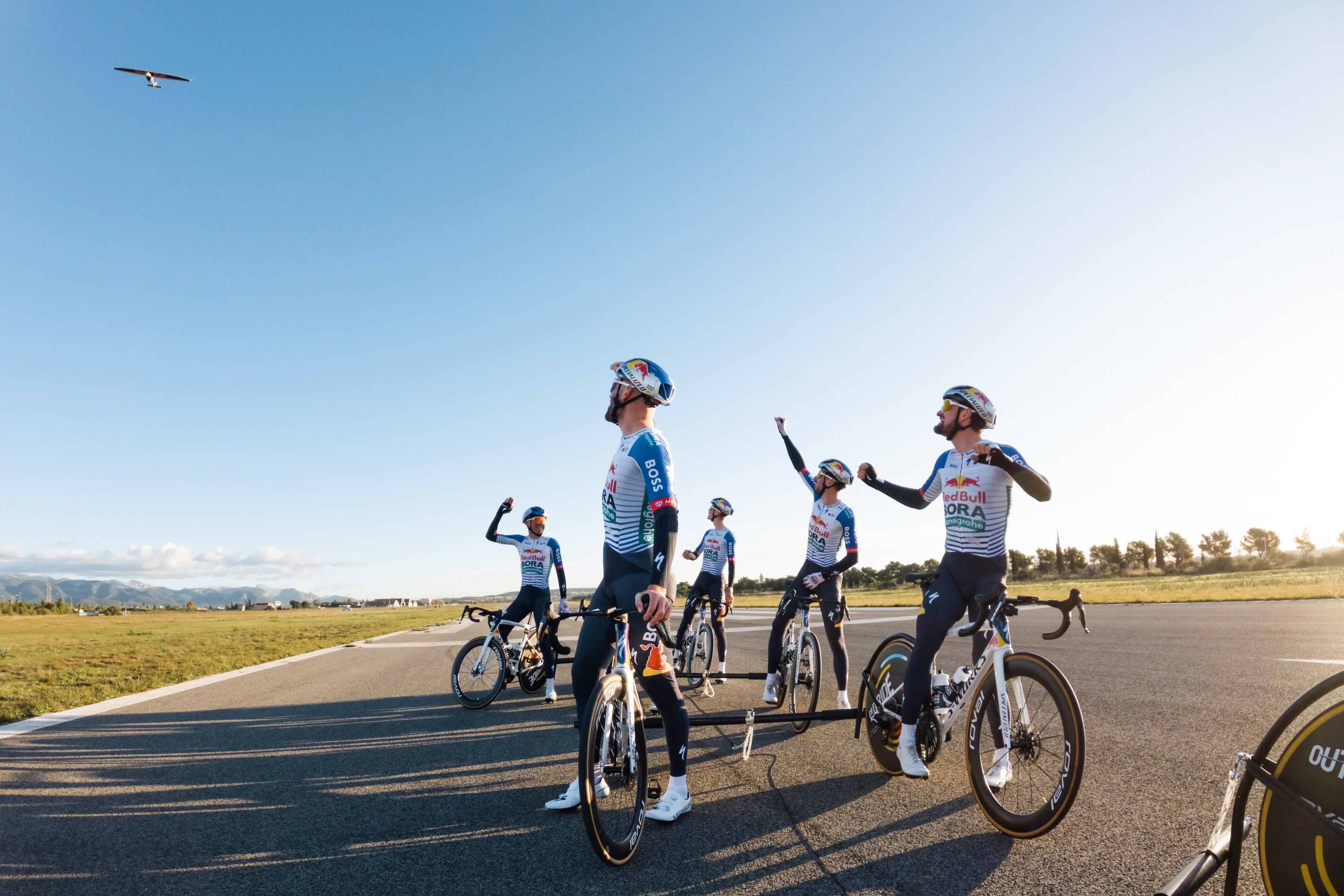 Red Bull-Bora-Hansgrohe riders look up at a glider plane that they launched