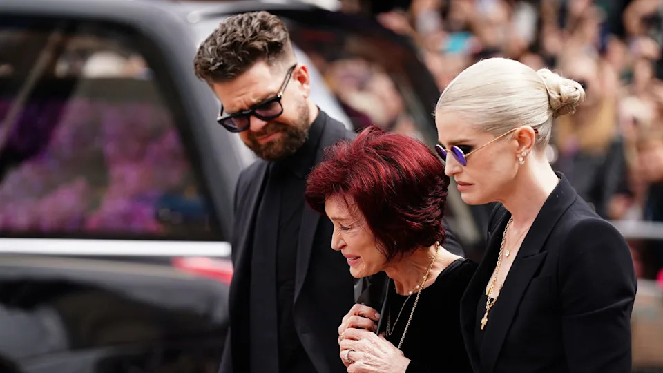From left, Jack, Sharon and Kelly Osbourne stand alongside Ozzy's funeral hearse, as they look at the floral tributes laid in the day's after the Black Sabbath frontman died, in July.