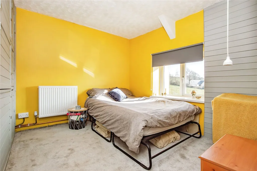 Bedroom with yellow wall, grey bedding, large window and view of grassy outdoor area.