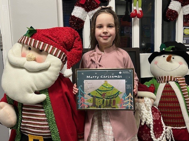 Emily Coomer with her winning christmas card design. She is standing in between a Father Christmas and snowman