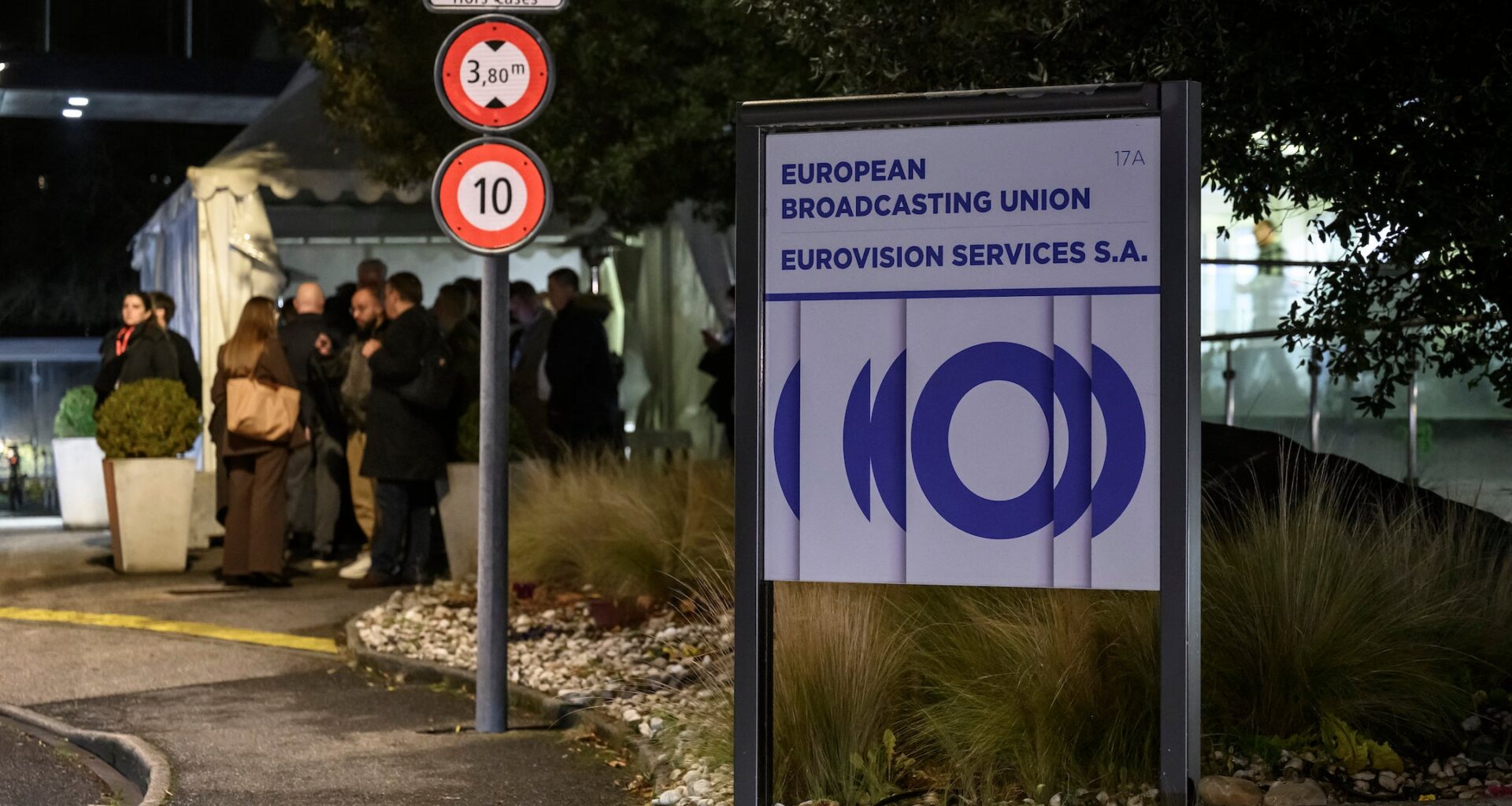 A photo of delegates standing behind a sign for the EBU headquarters.