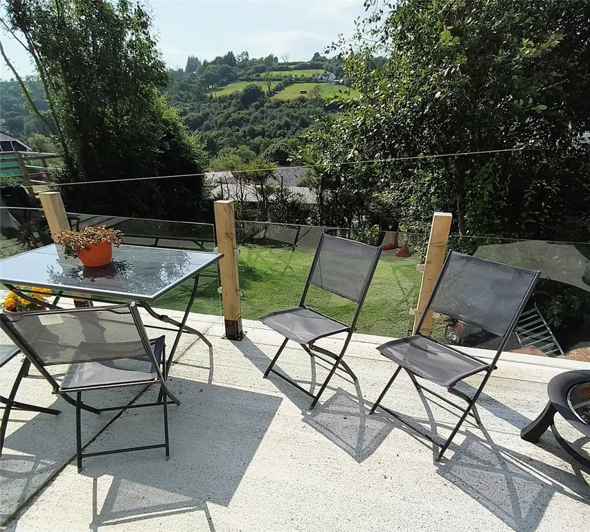Glass-top patio table with mesh chairs overlooking green hills and trees in Carmarthenshire.