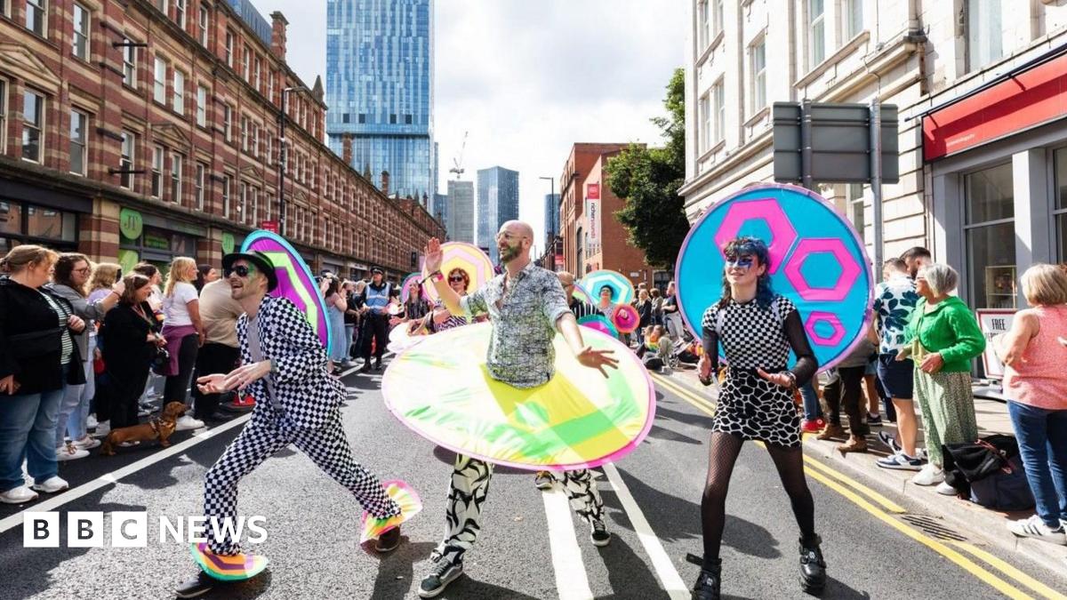 Three participants in a Manchester Pride parade. One wears a black trilby and black and white checked suit (left). The central marcher has a beard, black and white outfit with a multicoloured circle around the midriff while the person on the right has a multi patterned black and white dress  and dyed blue hair.