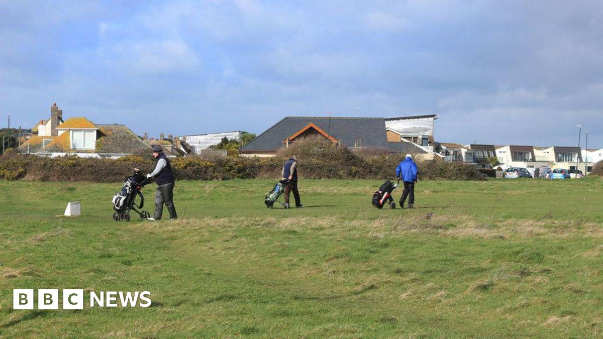 Three golfers with golf carts walking on the gold course at Solent Meads. In the background are neighbouring houses - large dormer bungalows with pitched roofs and two-storey modern houses with balconies.