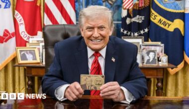 President Donald Trump smiles for the camera in the White House and he holds up a Trump Gold Card