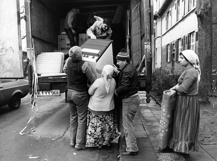 A group of people load luggage onto the back of a truck.