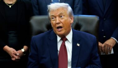 Donald Trump speaks while seated at a desk, surrounded by people, during the announcement of changes to fuel economy standards.