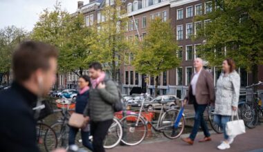 People walk across a bridge over the Keizersgracht canal in Amsterdam with bicycles parked nearby.