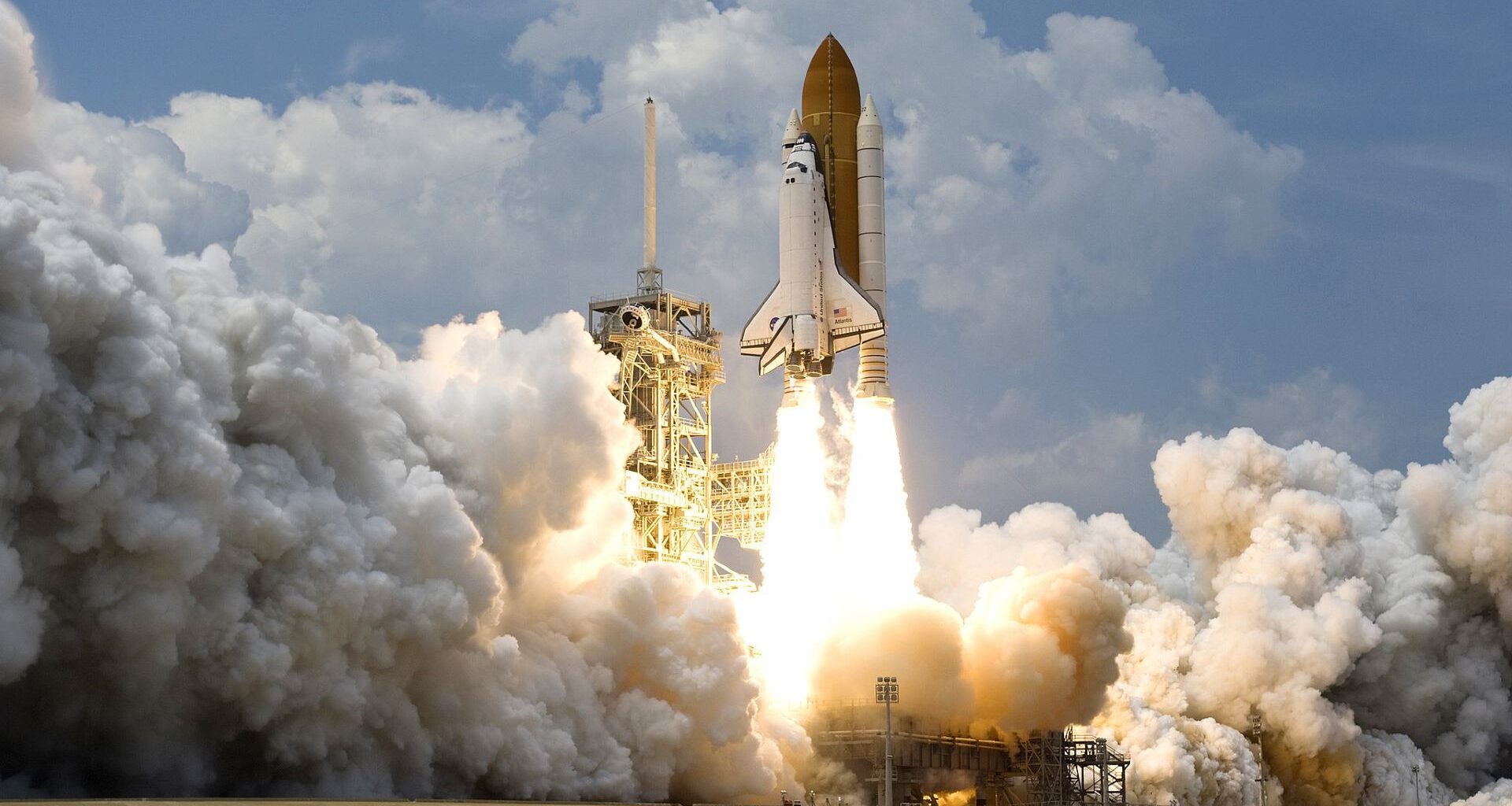 A white space shuttle launches off a pad with large clouds of smoke underneath it