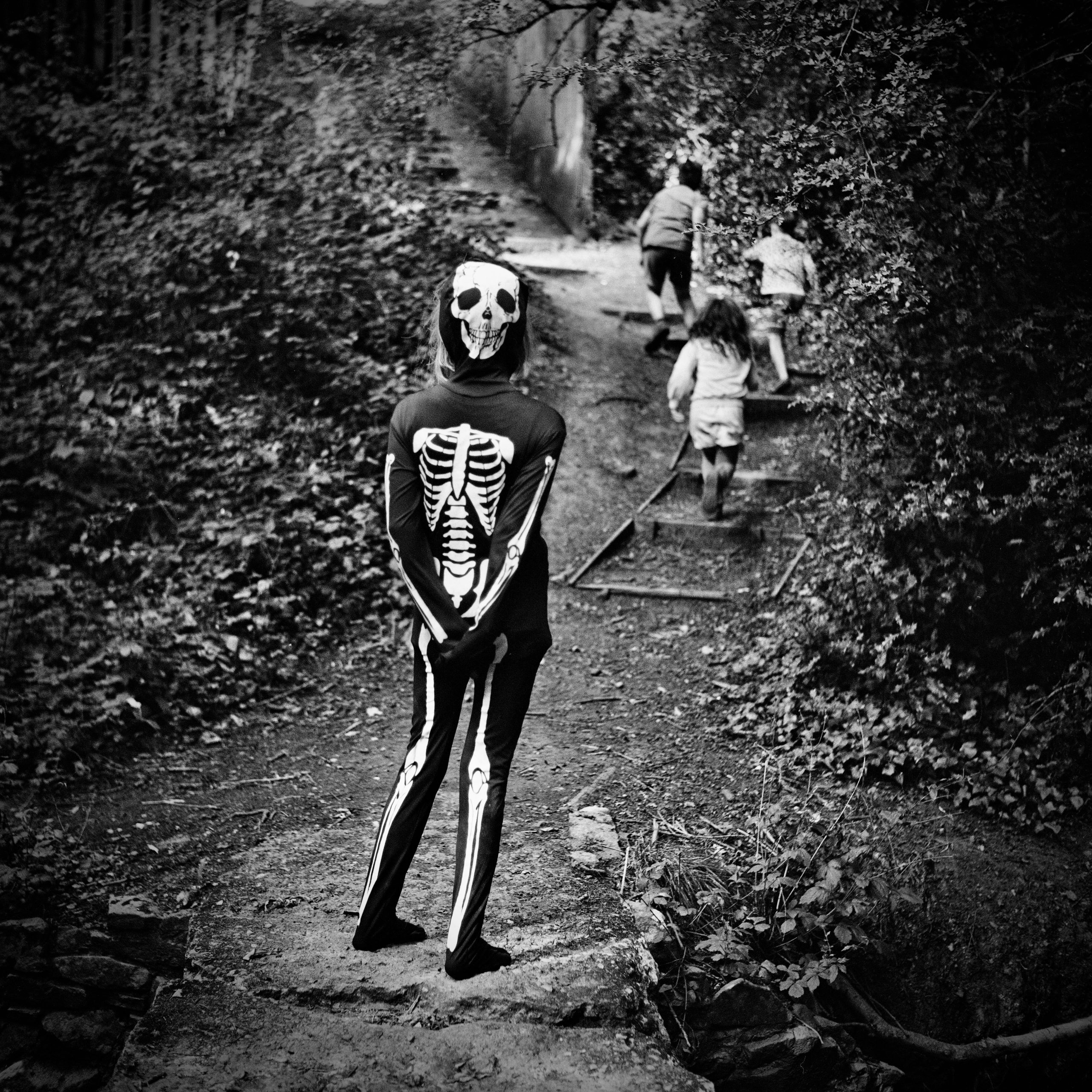 A girl in a skeleton costumer watches three other children run up steps in a park. 