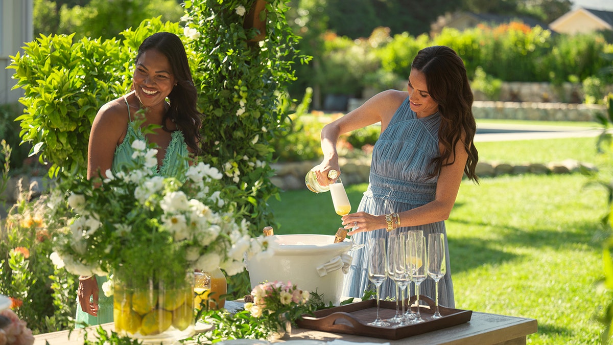 Meghan Markle in a sleeveless blue dress outdoors serving mimosas.