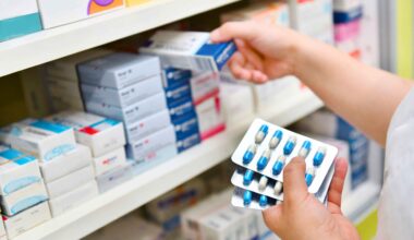 Person selecting medicine boxes from a pharmacy shelf while holding blister packs of capsules.