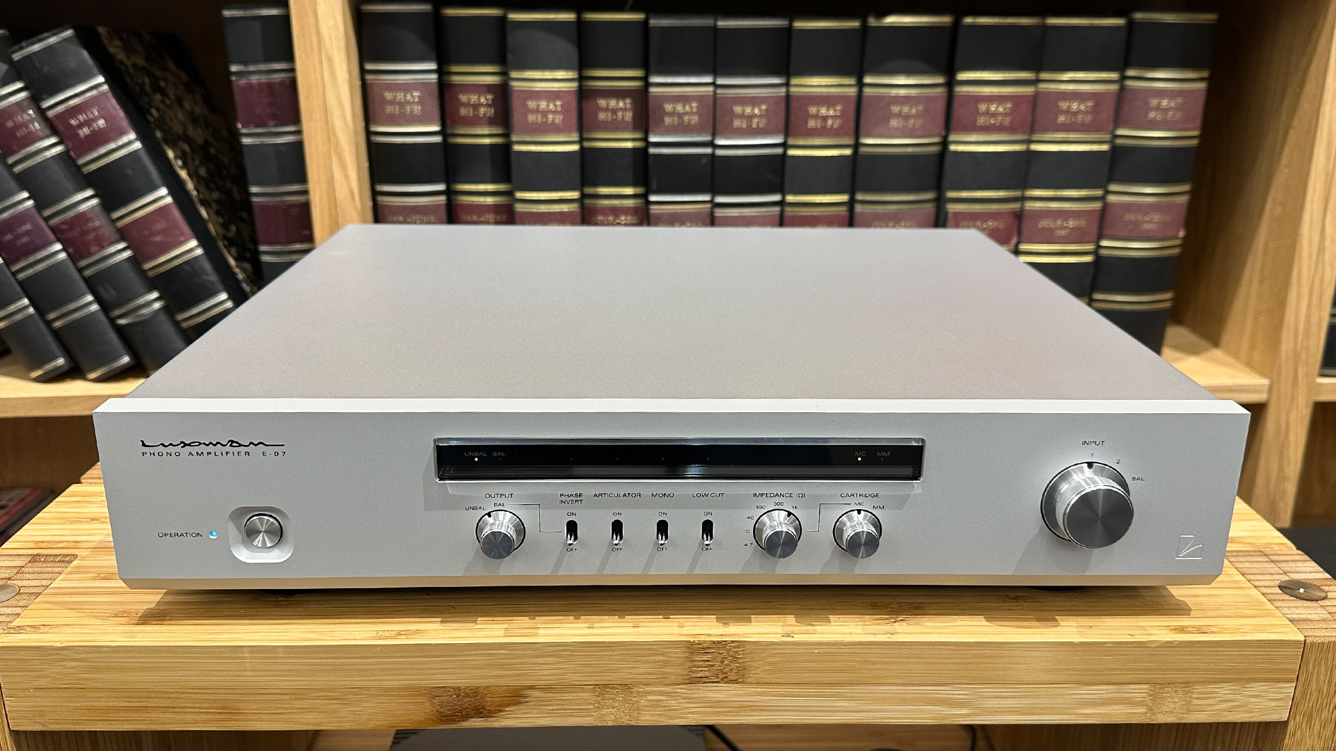 Luxman E-07 phono stage on wooden hi-fi rack in front of bookcase