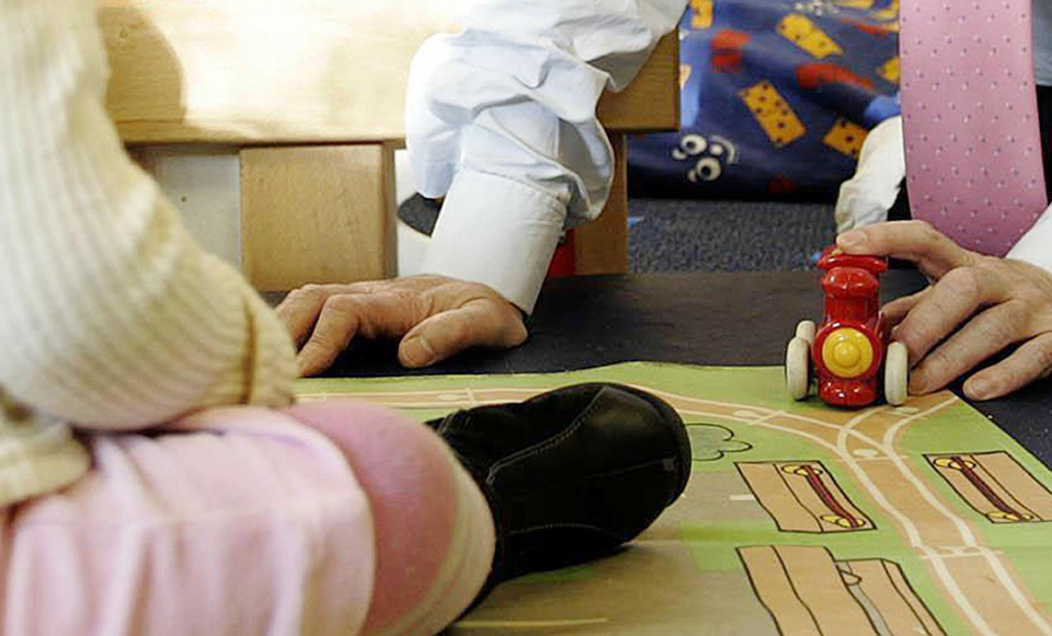 A baby's booted foot on a play mat with the hand of an adult in a shirt